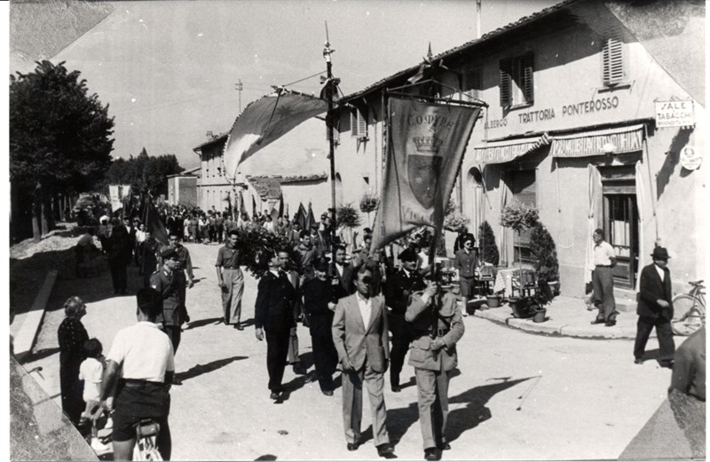 Un corteo (1954) torna in paese doppo essere stato alla Cappella dei partigiani al cimitero della Misericordia. Transita  davanti all’Albergo Ponterosso dove dieci anni prima lavorava Domenico Trifirò