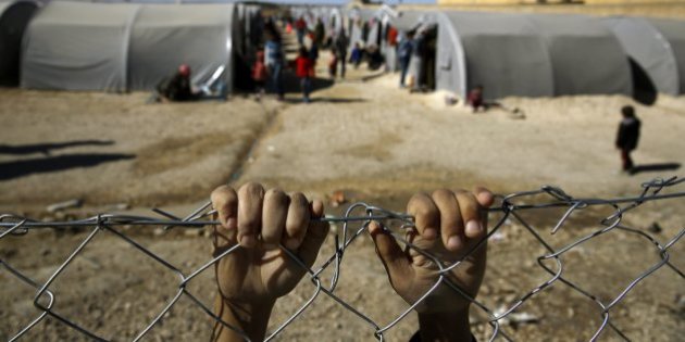 Kurdish refugee boy from the Syrian town of Kobani holds onto a fence that surrounds a refugee camp in the border town of Suruc, Sanliurfa province